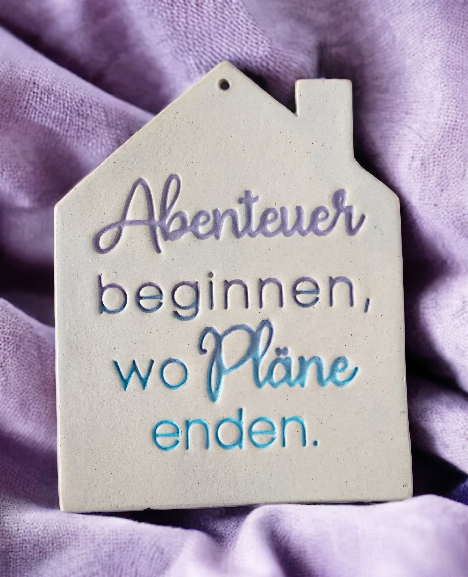 Handgefertigtes Keramik-Haus als Anhänger mit eingestempeltem Spruch. Die blau-violette Glasur betont das tiefe Relief des MinseArt Textstempels auf hellem Ton.