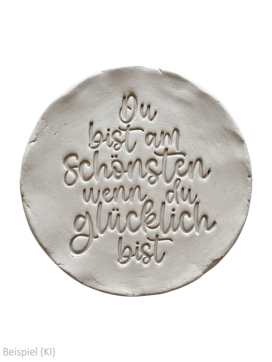 Freigestellter runder Tonabdruck mit dem tief geprägten Spruch Du bist am Schönsten wenn du glücklich bist auf schwarzem Hintergrund von MinseArt.