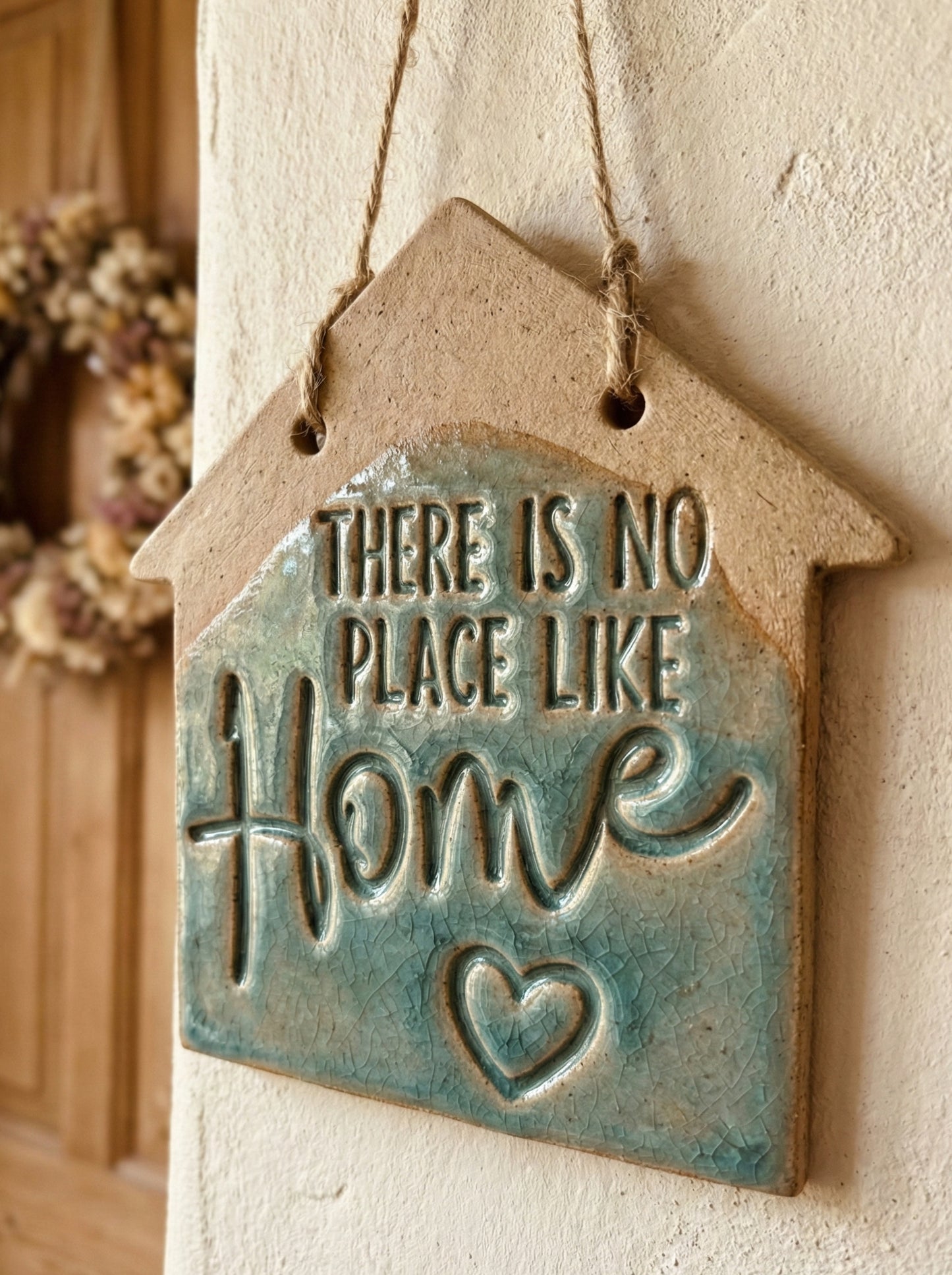 Glasiertes Keramikwandschild in Hausform mit dem Spruch 'There is no place like Home'. Die blaugrüne Craquelé-Glasur betont das tiefe Relief des MinseArt Keramikstempels.