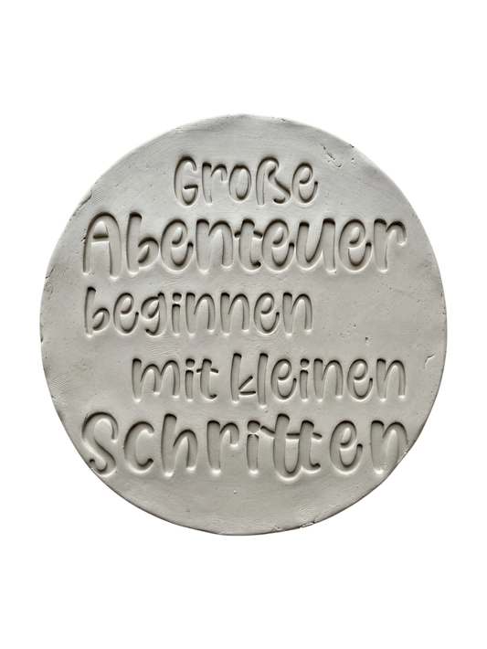 Detailreicher Abdruck im Ton mit dem Spruch 'Große Abenteuer beginnen mit kleinen Schritten'. Erstellt mit einem MinseArt Keramikstempel. Saubere Schriftzüge und präzise Konturen für deine nächste Töpfer-Idee im Bereich Baby-Geschenke und Kinderzimmer-Deko.