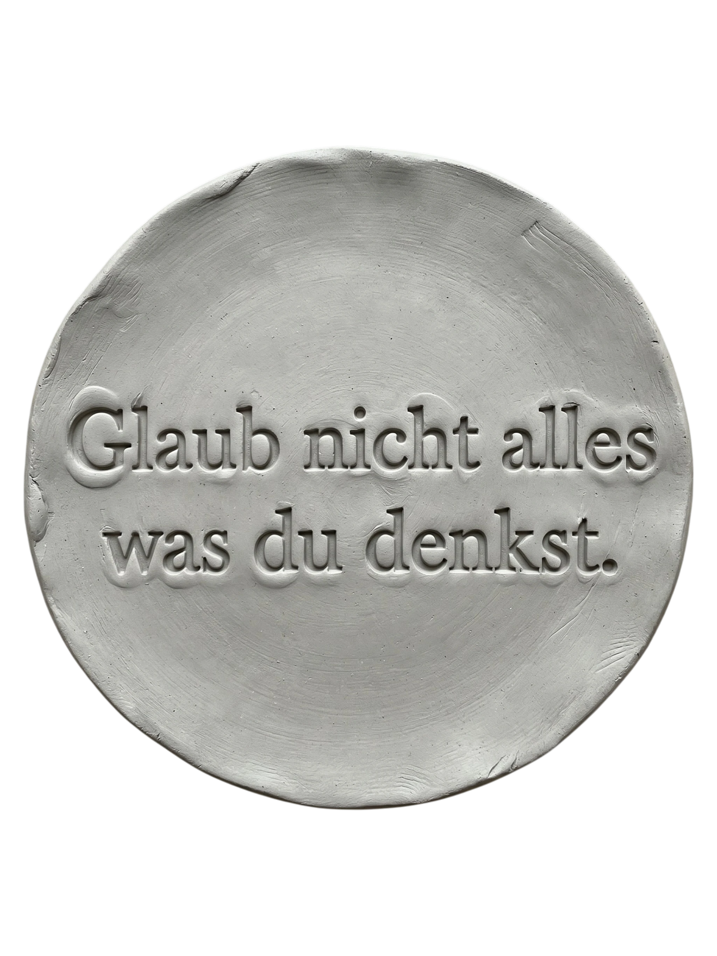 Präziser Stempelabdruck 'Glaub nicht alles was du denkst' in hellem Ton. Sauberes, tiefes Relief auf einer runden Tonplatte, erstellt mit einem MinseArt Textstempel.