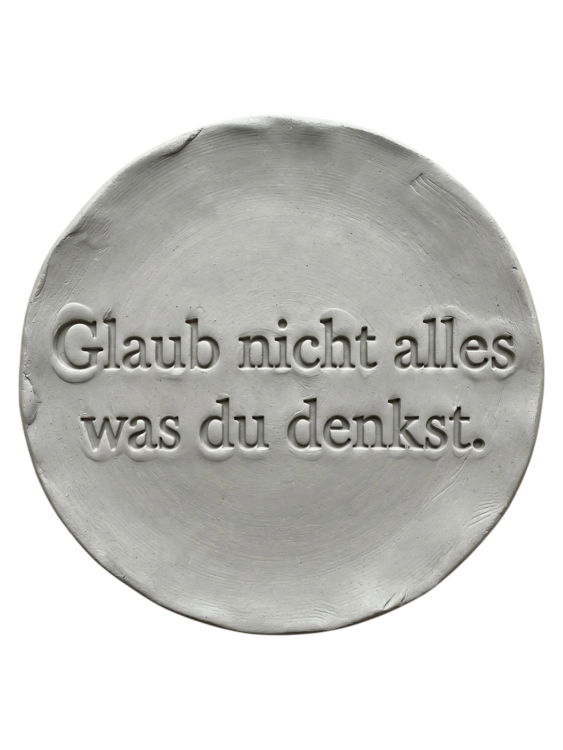 Präziser Stempelabdruck 'Glaub nicht alles was du denkst' in hellem Ton. Sauberes, tiefes Relief auf einer runden Tonplatte, erstellt mit einem MinseArt Textstempel.