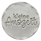 Präziser Stempelabdruck 'kleine Auszeit' in hellem Ton. Das saubere Relief kombiniert eine moderne Serifenschrift mit eleganter Schreibschrift auf einer runden Tonplatte.
