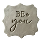 Präziser Abdruck im hellen Ton mit der Botschaft 'BE you' auf einer dekorativ geformten Tonplatte. Kreative Töpfer-Idee für Motivations-Schilder oder Wand-Deko.
