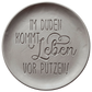 Witziger Stempelabdruck 'Im Duden kommt Leben vor Putzen' in hellem Ton. Sauberes Relief mit einer Kombination aus moderner Druckschrift und schwungvoller Schreibschrift.