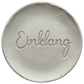 Präziser Stempelabdruck des Wortes 'Einklang' in eleganter Schreibschrift auf einer runden Tonplatte. Filigranes Relief für spirituelle Keramik, gestaltet mit einem MinseArt Keramikstempel.