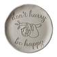 Präziser Stempelabdruck eines Faultiers mit dem Schriftzug 'don't hurry be happy' in hellem Ton. Sauberes Relief für die Gestaltung von Tellern und Schalen.