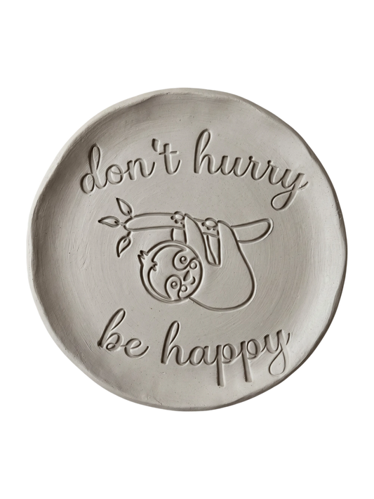 Präziser Stempelabdruck eines Faultiers mit dem Schriftzug 'don't hurry be happy' in hellem Ton. Sauberes Relief für die Gestaltung von Tellern und Schalen.