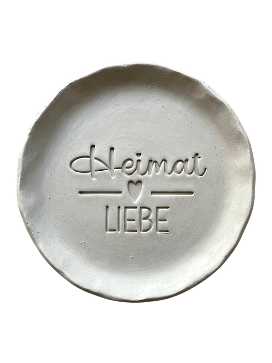 Sauberer Abdruck im hellen Ton mit dem Spruch 'Heimat Liebe'. Kreative Töpfer-Idee für regionale Wandteller, Türschilder oder rustikale Deko.
