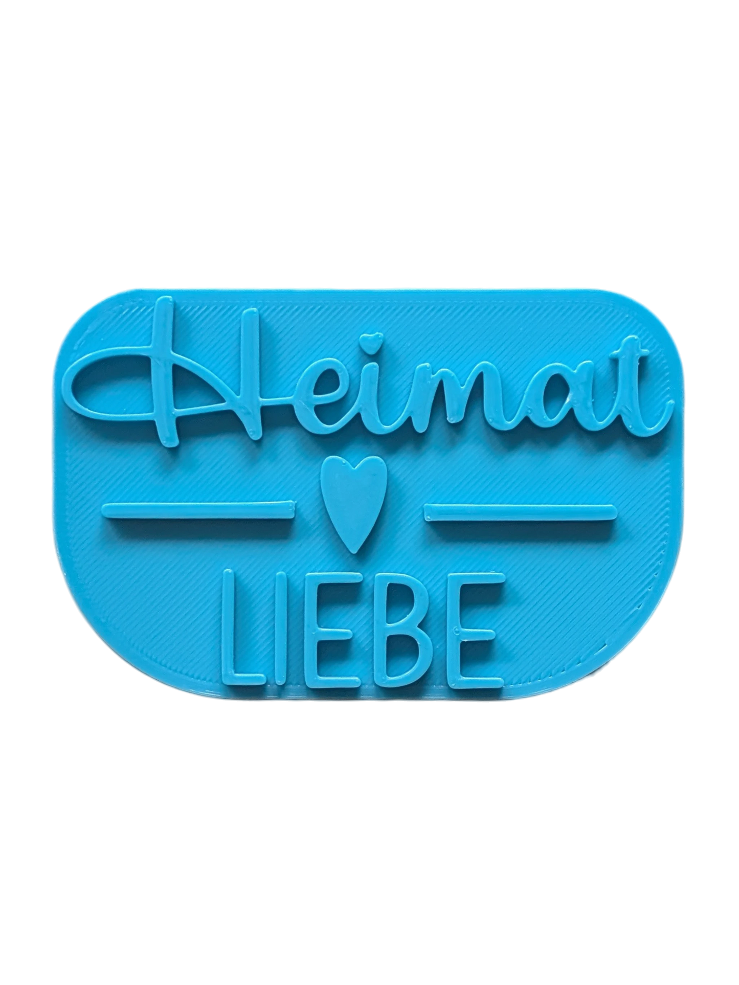Draufsicht auf den Keramikstempel für Ton mit dem Schriftzug 'Heimatliebe'. Ein detailreicher Tonstempel, kombiniert aus Schreibschrift und Druckbuchstaben mit einem kleinen Herz.