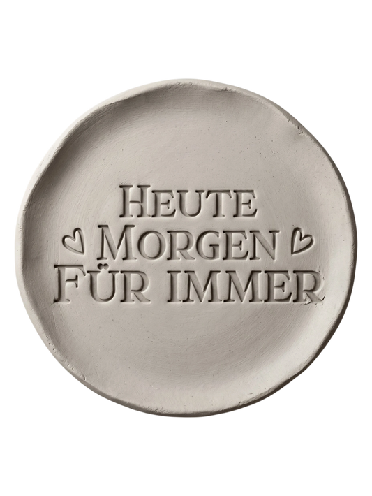 Präziser Stempelabdruck des romantischen Spruchs 'Heute Morgen Für Immer' in hellem Ton. Detailreiches, sauberes Relief in klassischer Druckschrift mit kleinen Herzen auf einer runden Tonplatte.