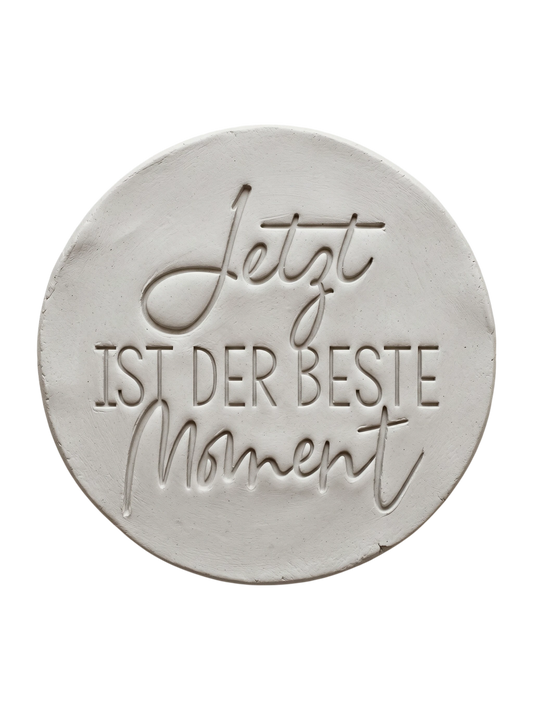 Präziser Stempelabdruck 'Jetzt ist der beste Moment' in hellem Ton. Die harmonische Kombination aus schwungvoller Kalligrafie und klarer Serifenschrift erzeugt ein tiefes Relief.