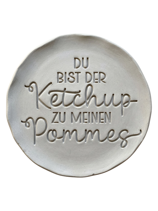 Ein glasierter Keramikteller mit dem handgemachten Stempelabdruck 'Du bist der Ketchup zu meinen Pommes'. Detailreicher Schriftzug und eine kleine Pommesschachtel als Verzierung für kreative Töpferprojekte.
