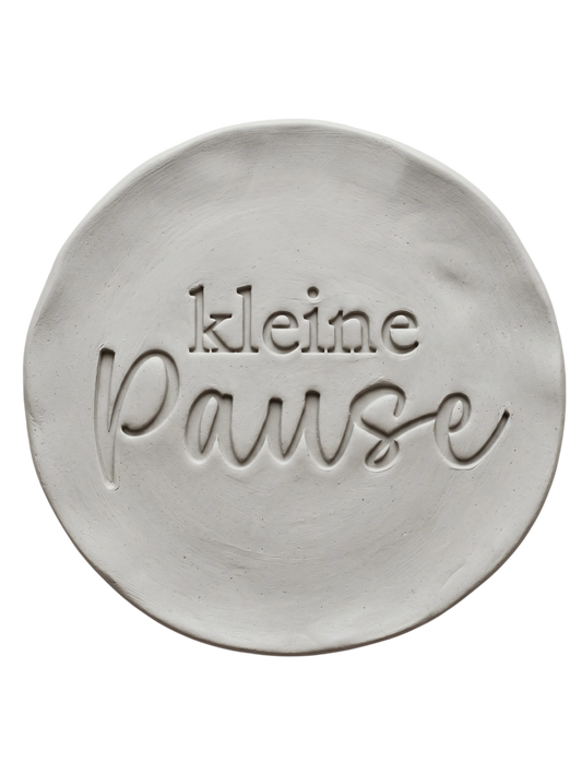 Präziser Stempelabdruck 'kleine Pause' in hellem Ton. Die Kombination aus moderner Druckschrift und eleganter Schreibschrift erzeugt ein sauberes Relief auf der runden Tonplatte.