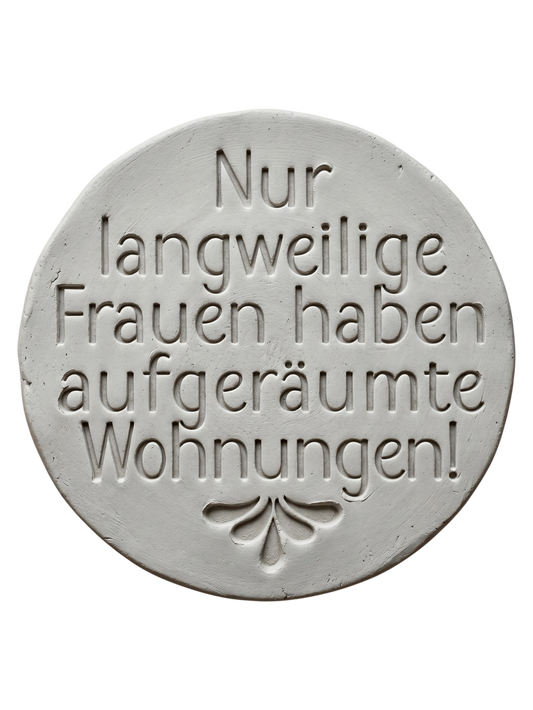 Präziser Stempelabdruck 'Nur langweilige Frauen haben aufgeräumte Wohnungen!' in hellem Ton. Sauberes Relief mit moderner Typografie und floralem Ornament am unteren Rand.