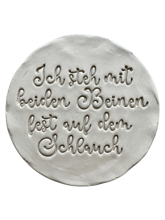Präziser Stempelabdruck in hellem Ton. Die verspielte Schreibschrift erzeugt ein sauberes, tiefes Relief auf der runden Tonplatte – ideal für witzige Keramik-Deko.