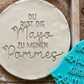 Ein sauberer Stempelabdruck des Spruchs 'Du bist die Mayo zu meinen Pommes' in einer runden Tonplatte. Daneben liegt der türkisfarbene MinseArt Keramikstempel auf einem rustikalen Holztisch zusammen mit Töpferwerkzeug und Abstandshaltern für die perfekte Plattendicke.