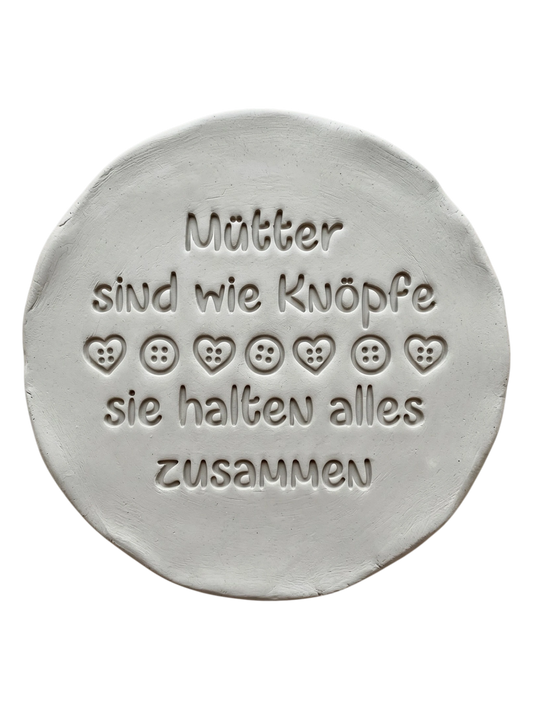 Liebevolle Töpfer-Idee zum Muttertag: Ton-Anhänger mit dem eingestempelten Spruch 'Mütter sind wie Knöpfe, sie halten alles zusammen'. Erstellt mit einem MinseArt Keramikstempel. Präziser Abdruck mit Herz- und Knopf-Details in hellem Ton.