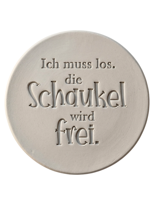 Präziser Stempelabdruck des humorvollen Spruchs 'Ich muss los. die Schaukel wird frei.' in hellem Ton. Das saubere Relief kombiniert klassische Serifenschrift mit verspielten Details auf einer runden Tonplatte.