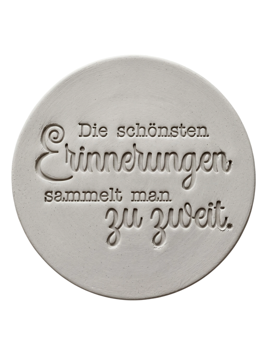 Präziser Stempelabdruck des romantischen Spruchs 'Die schönsten Erinnerungen sammelt man zu zweit' in hellem Ton. Detailreiches, sauberes Relief aus Schreibmaschinenschrift und Kalligrafie auf einer runden Tonplatte.