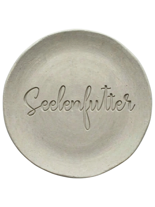Eleganter Stempelabdruck in Schreibschrift mit dem Wort 'Seelenfutter' auf einem runden Tonteller. Hochwertiges Relief-Ergebnis für Keramikprojekte, erstellt mit einem MinseArt Keramikstempel.