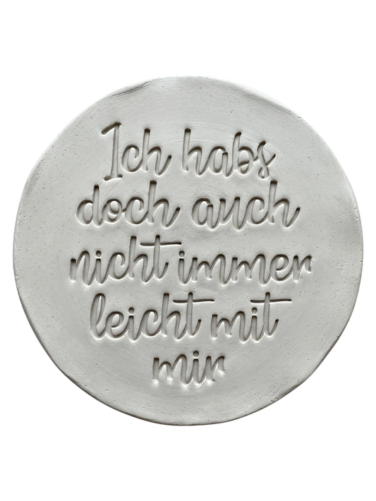 Präziser Stempelabdruck in hellem Ton. Die schwungvolle Handschrift erzeugt ein sauberes Relief auf der runden Tonplatte. Ideal für witzige Keramik-Geschenke.