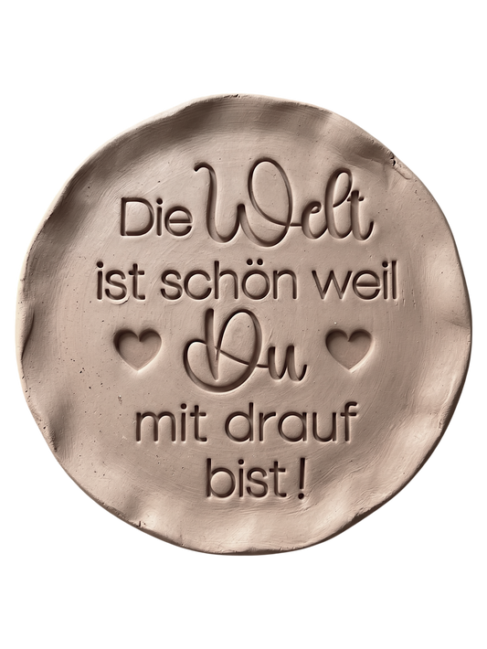 Perfekter Abdruck im Ton mit dem Spruch 'Die Welt ist schön weil Du mit drauf bist!'. Erstellt mit einem MinseArt Keramikstempel. Eine kreative Töpfer-Idee für Geschenke an Lieblingsmenschen, mit präzisen Konturen und feinen Herz-Details.