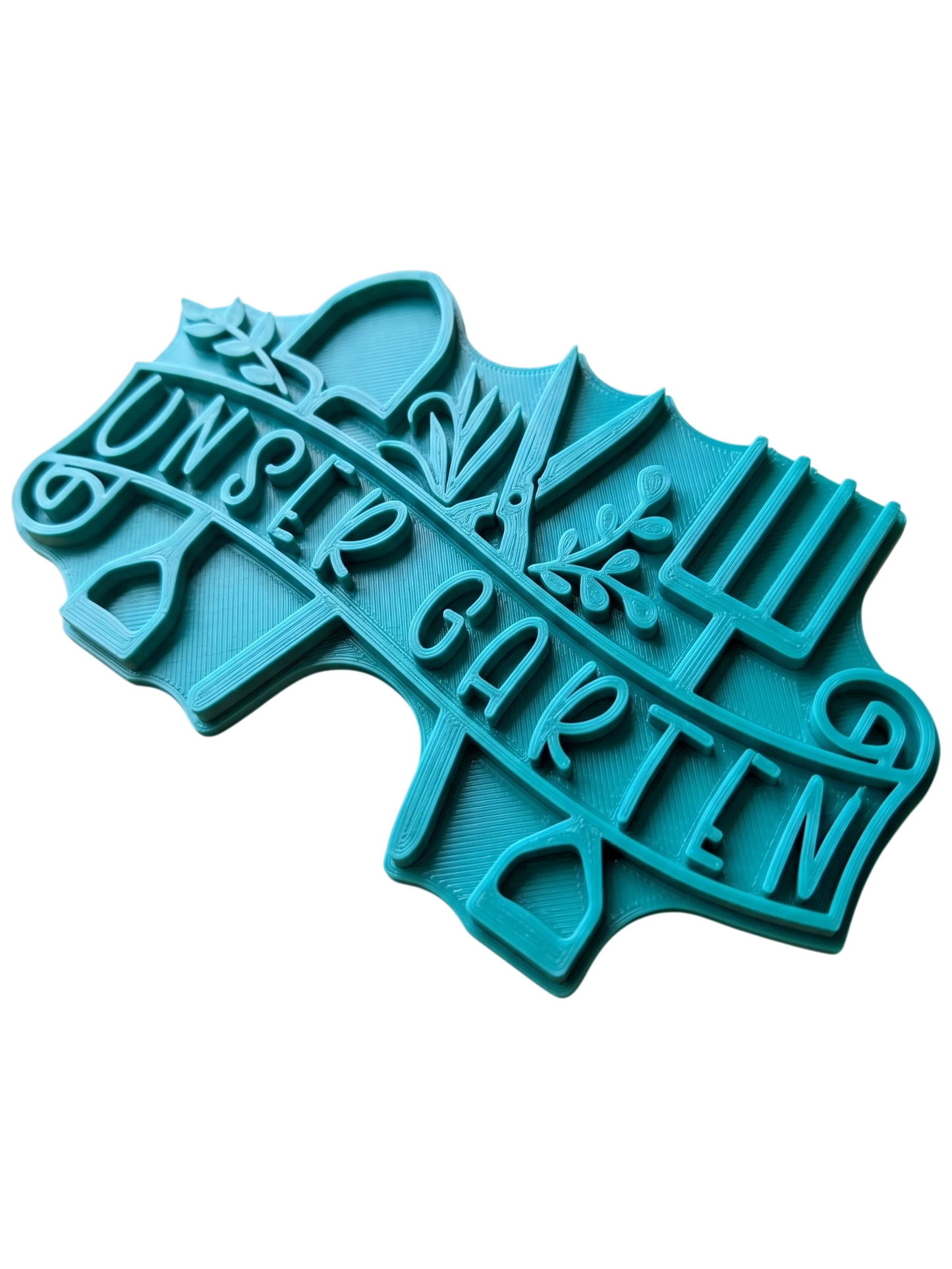 Türkisfarbener Keramikstempel für Ton mit dem Schriftzug "unser Garten" auf einem Banner, umrahmt von Schaufel, Gartenschere und Grabegabel. Detailreicher Prägestempel für kreative Töpfer-Ideen.