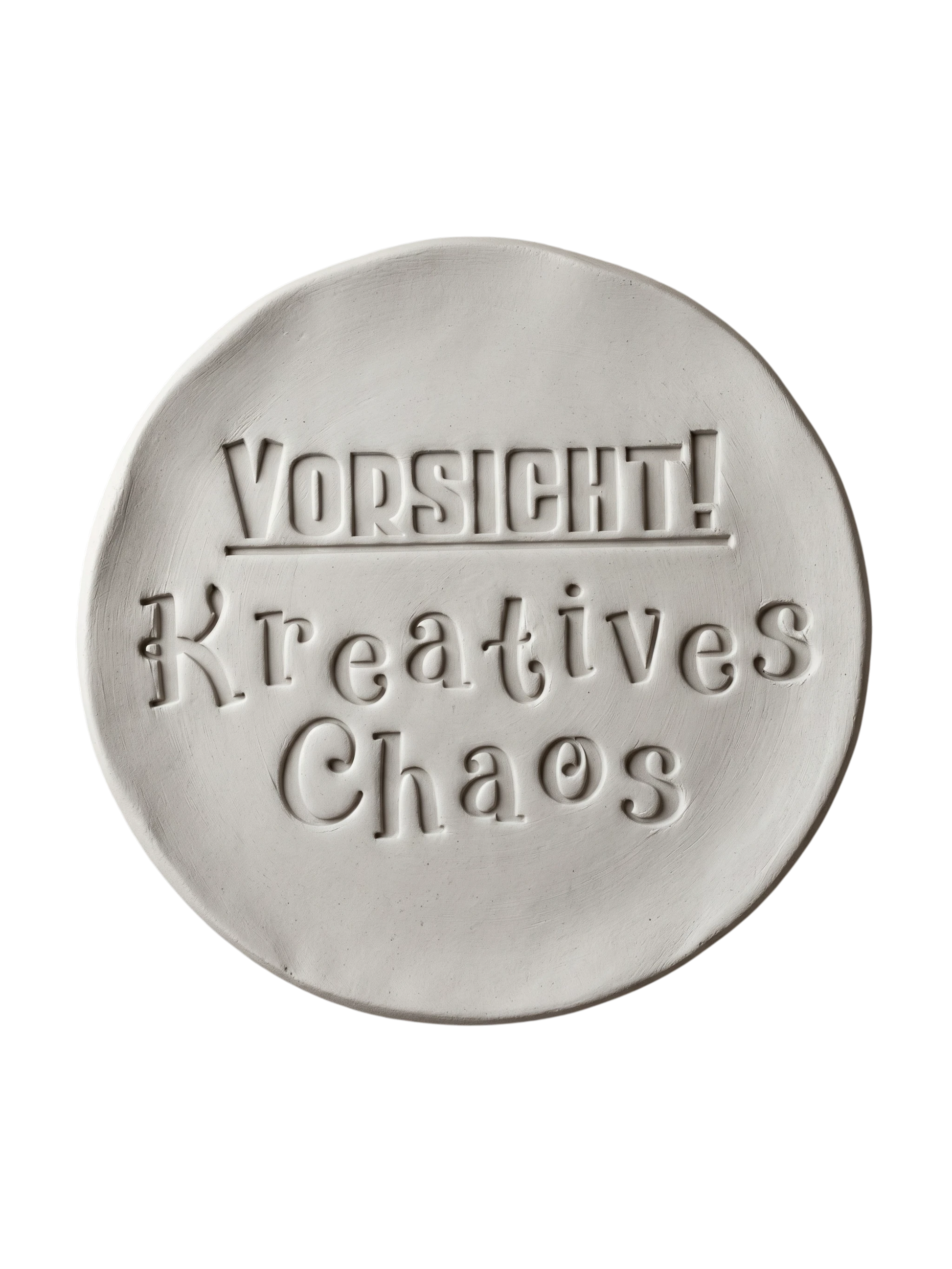Sauberer Stempelabdruck 'Vorsicht! Kreatives Chaos' in hellem Ton. Die verspielte Typografie mit dekorativen Serifen erzeugt ein präzises Relief auf der runden Tonplatte.
