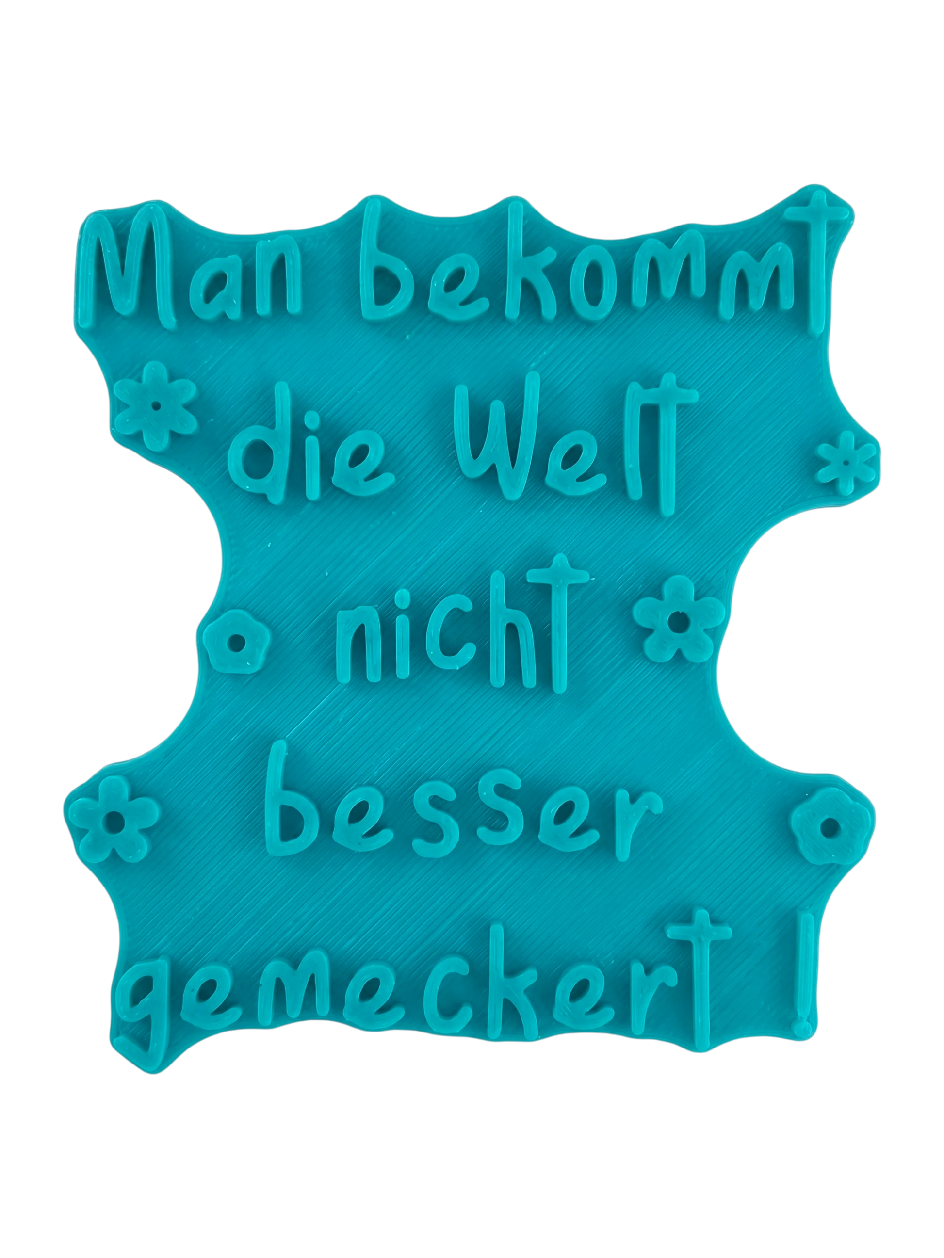 Türkisfarbener Keramikstempel für Ton mit dem Schriftzug 'Man bekommt die Welt nicht besser gemeckert!'. Hochwertiges Töpferwerkzeug für originelle und humorvolle Keramikprojekte.