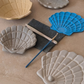 Muschel-Prägeplatte aus blauem Material drapiert neben fertig geformten Muschelschalen und Töpferzubehör.