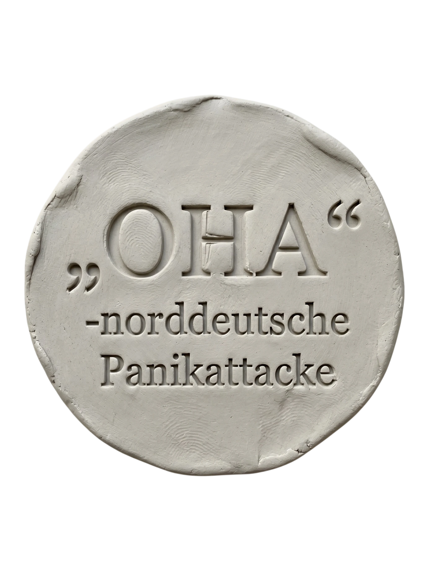 Präziser Stempelabdruck des witzigen Spruchs 'OHA - norddeutsche Panikattacke' in hellem Ton. Sauberes, tiefes Relief mit klarer Typografie auf einer runden Tonplatte.