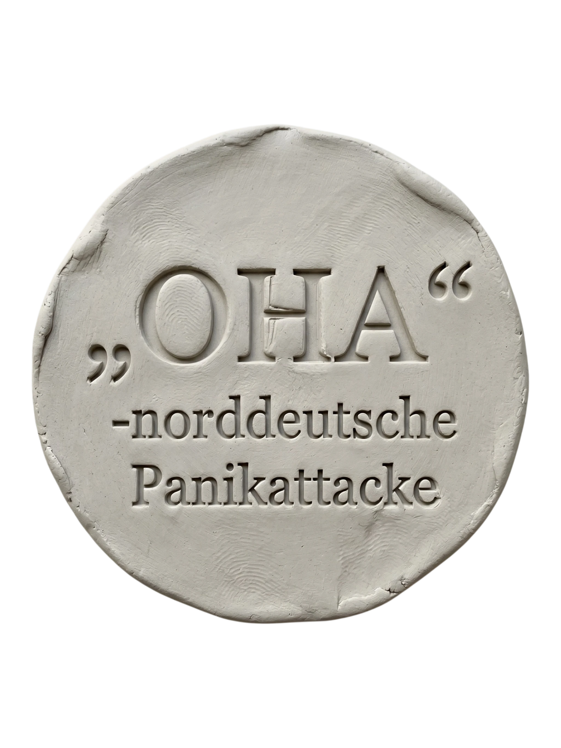 Präziser Stempelabdruck des witzigen Spruchs 'OHA - norddeutsche Panikattacke' in hellem Ton. Sauberes, tiefes Relief mit klarer Typografie auf einer runden Tonplatte.