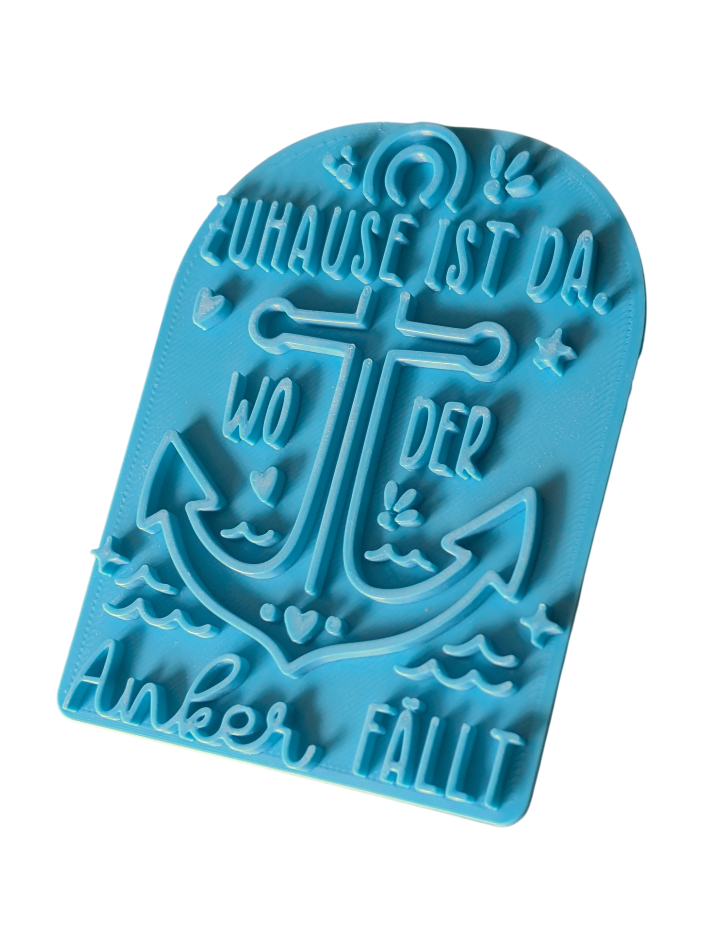 Schrägansicht des türkisfarbenen Prägestempels 'Zuhause ist da, wo der Anker fällt'. Ein hochwertiger Textstempel mit Anker-Motiv für maritime Töpfer-Projekte.