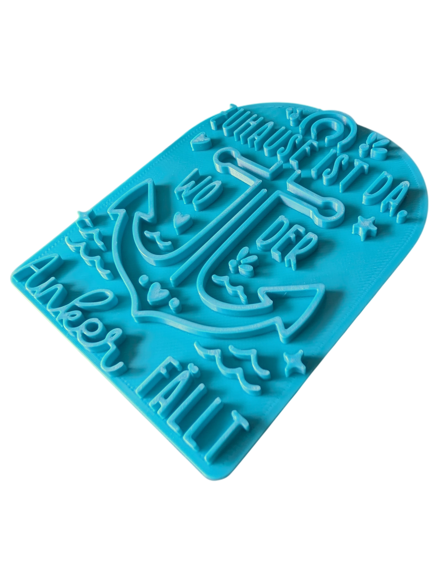 Schrägansicht des türkisfarbenen Prägestempels 'Zuhause ist da, wo der Anker fällt'. Ein hochwertiger Textstempel mit Anker-Motiv für maritime Töpfer-Projekte.