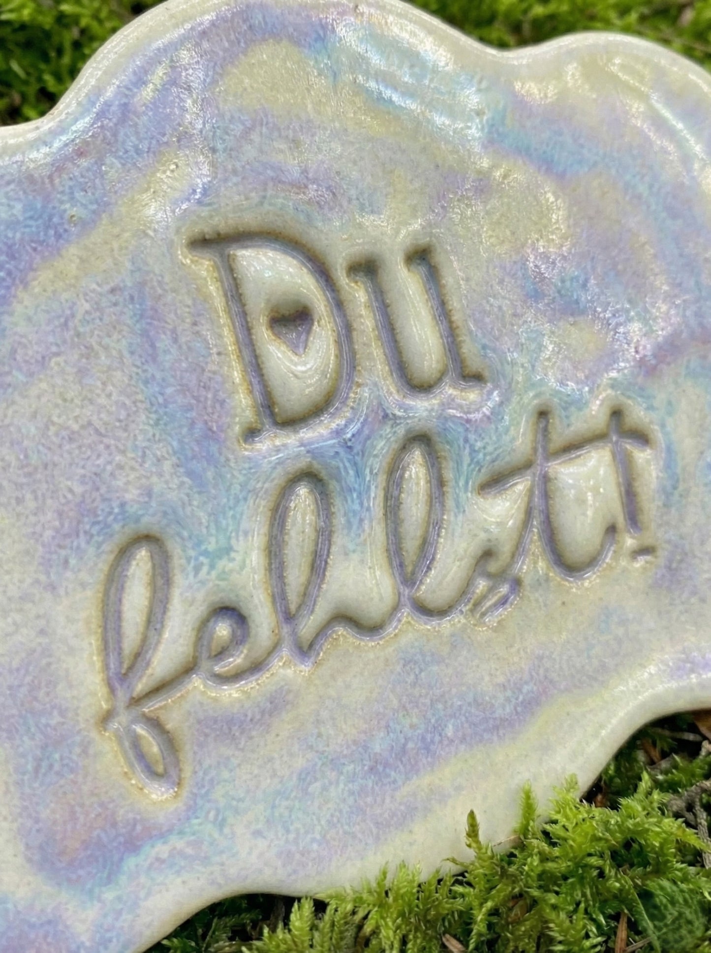 Nahaufnahme des glasierten Tonstempel-Abdrucks 'Du fehlst!'. Die sanft fließende Glasur betont die scharfen Konturen und das kleine Herz, die der Textstempel in der Keramik hinterlassen hat.