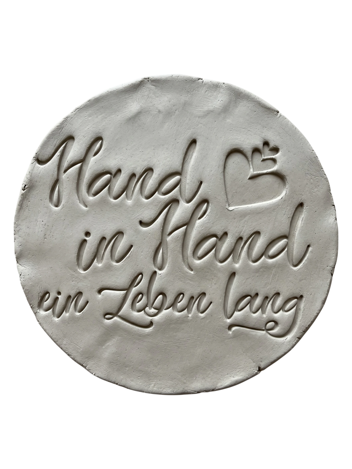 Präziser Stempelabdruck des Spruchs 'Hand in Hand ein Leben lang' in hellem Ton. Detailreiches, sauberes Relief in eleganter Schreibschrift mit Herzen auf einer runden Tonplatte. Handgefertigt mit einem MinseArt Textstempel.
