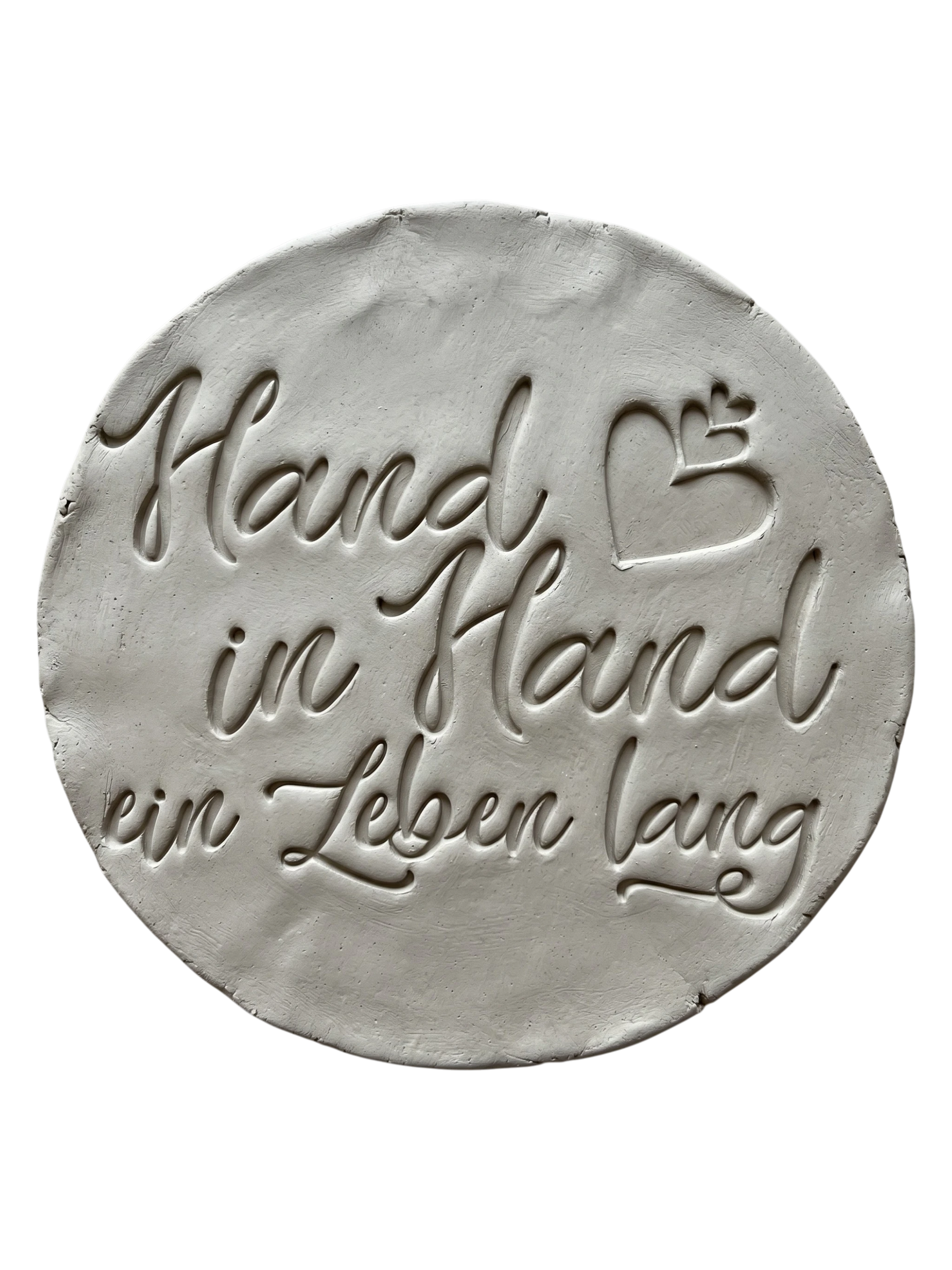 Präziser Stempelabdruck des Spruchs 'Hand in Hand ein Leben lang' in hellem Ton. Detailreiches, sauberes Relief in eleganter Schreibschrift mit Herzen auf einer runden Tonplatte. Handgefertigt mit einem MinseArt Textstempel.