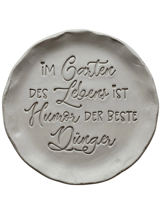 Präziser und sauberer Stempelabdruck des humorvollen Gartenspruchs in hellem Ton. Das tiefe Relief vereint Druck- und Schreibschrift auf einer runden Tonplatte.