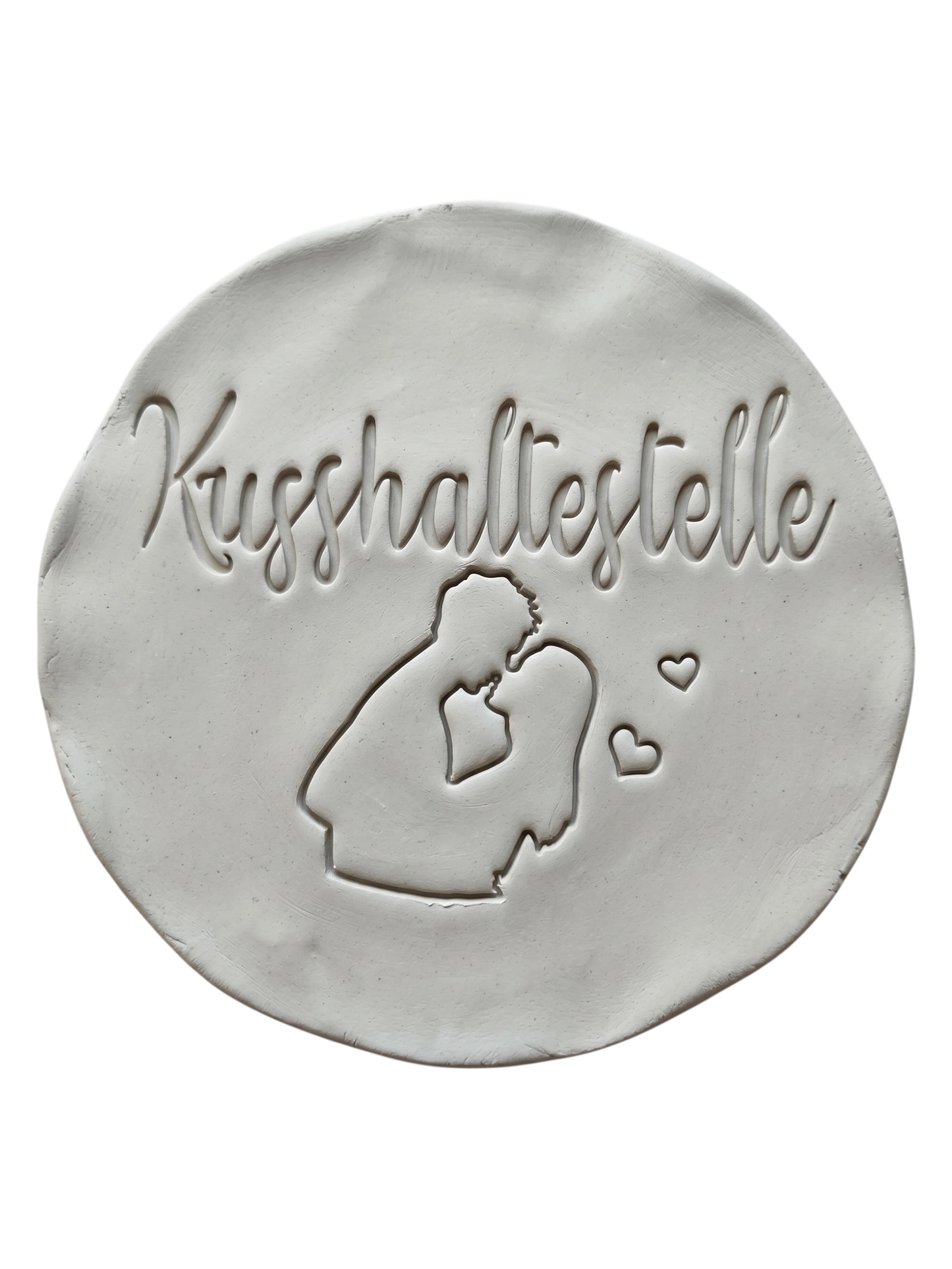 Sauberer und präziser Stempelabdruck des Motivs Kusshaltestelle in hellem Ton. Das detailreiche Relief zeigt ein küssendes Paar und kleine Herzen auf einer runden Tonplatte.