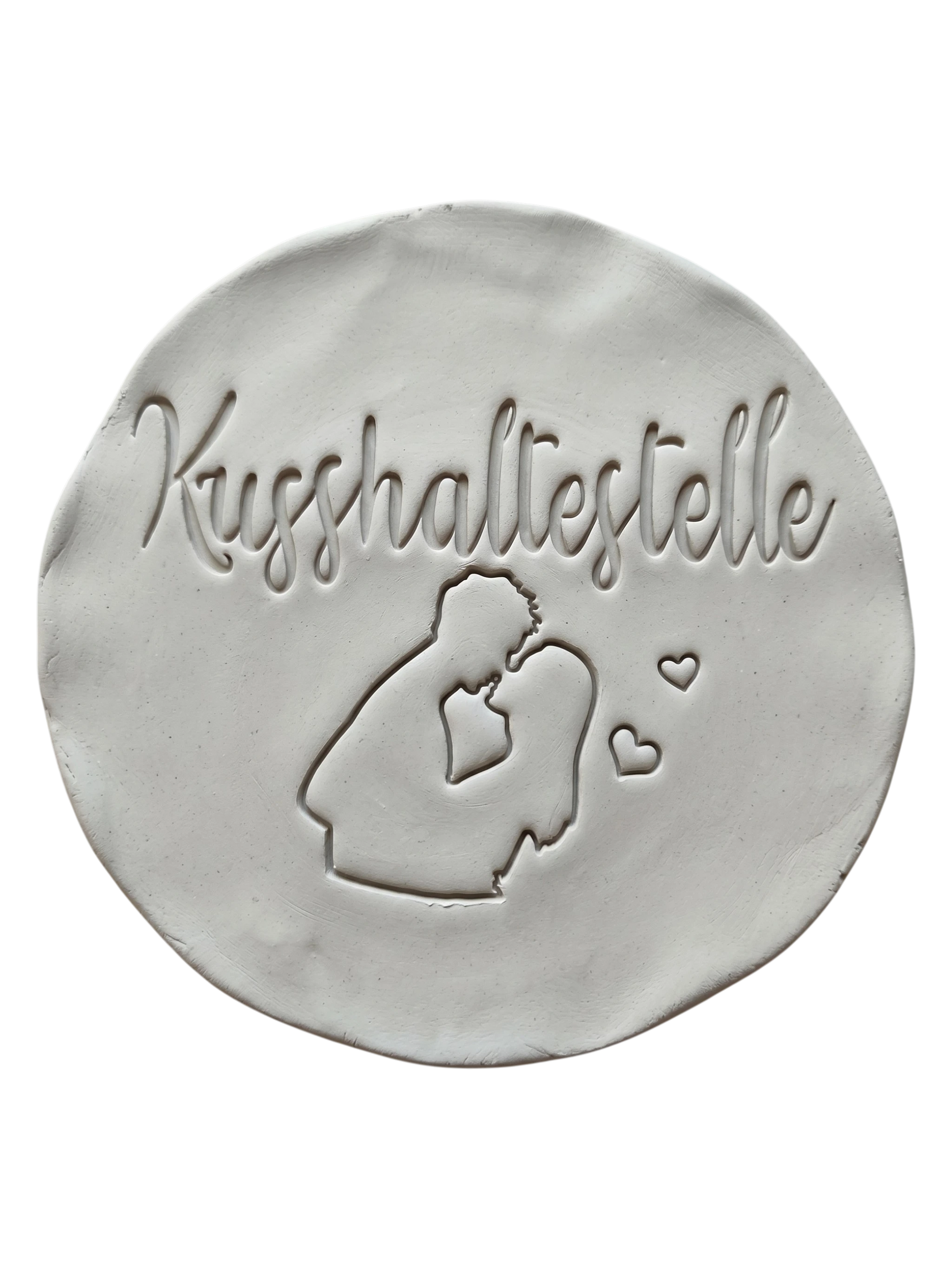 Sauberer und präziser Stempelabdruck des Motivs Kusshaltestelle in hellem Ton. Das detailreiche Relief zeigt ein küssendes Paar und kleine Herzen auf einer runden Tonplatte.