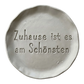 Detailreicher Stempelabdruck des Spruchs Zuhause ist es am Schönsten in hellem Ton. Das saubere Relief auf der runden Tonplatte zeigt präzise Konturen für dekorative Keramikprojekte.