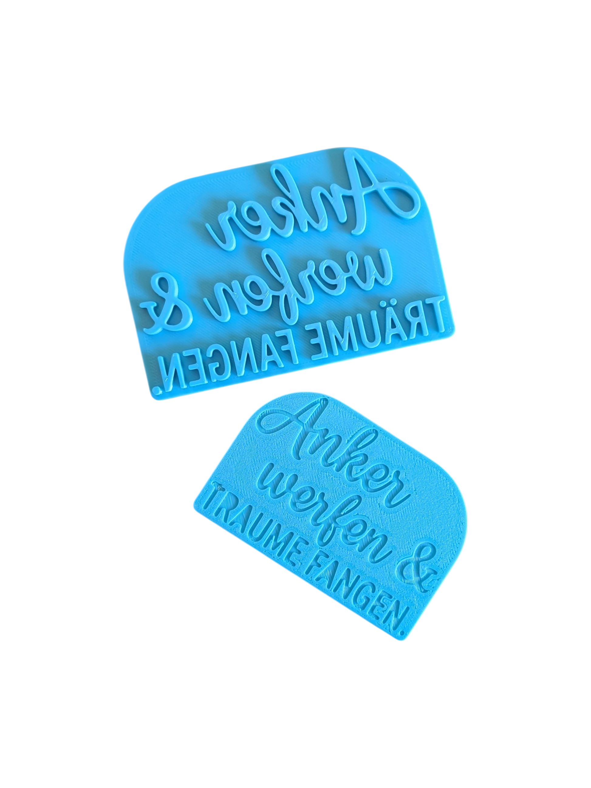 Draufsicht auf den türkisfarbenen Prägestempel für Ton mit dem Spruch 'Anker werfen & TRÄUME FANGEN.'. Ein maritimer Textstempel mit tiefem Relief für Keramik. Mit Positionierungshilfe auf der Rückseite