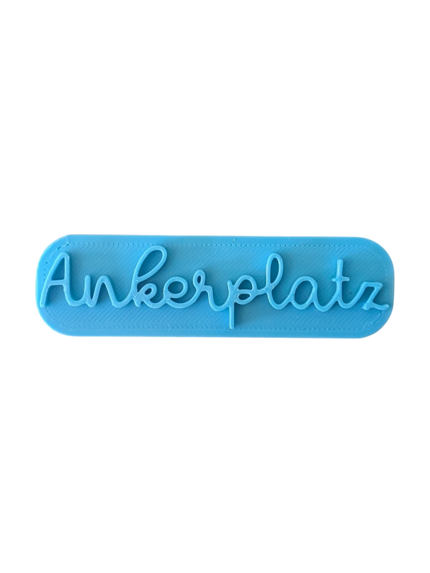 Draufsicht auf den türkisfarbenen Prägestempel für Ton mit dem Schriftzug 'Ankerplatz'. Ein eleganter Textstempel für maritim dekorierte Keramik und Türschilder.