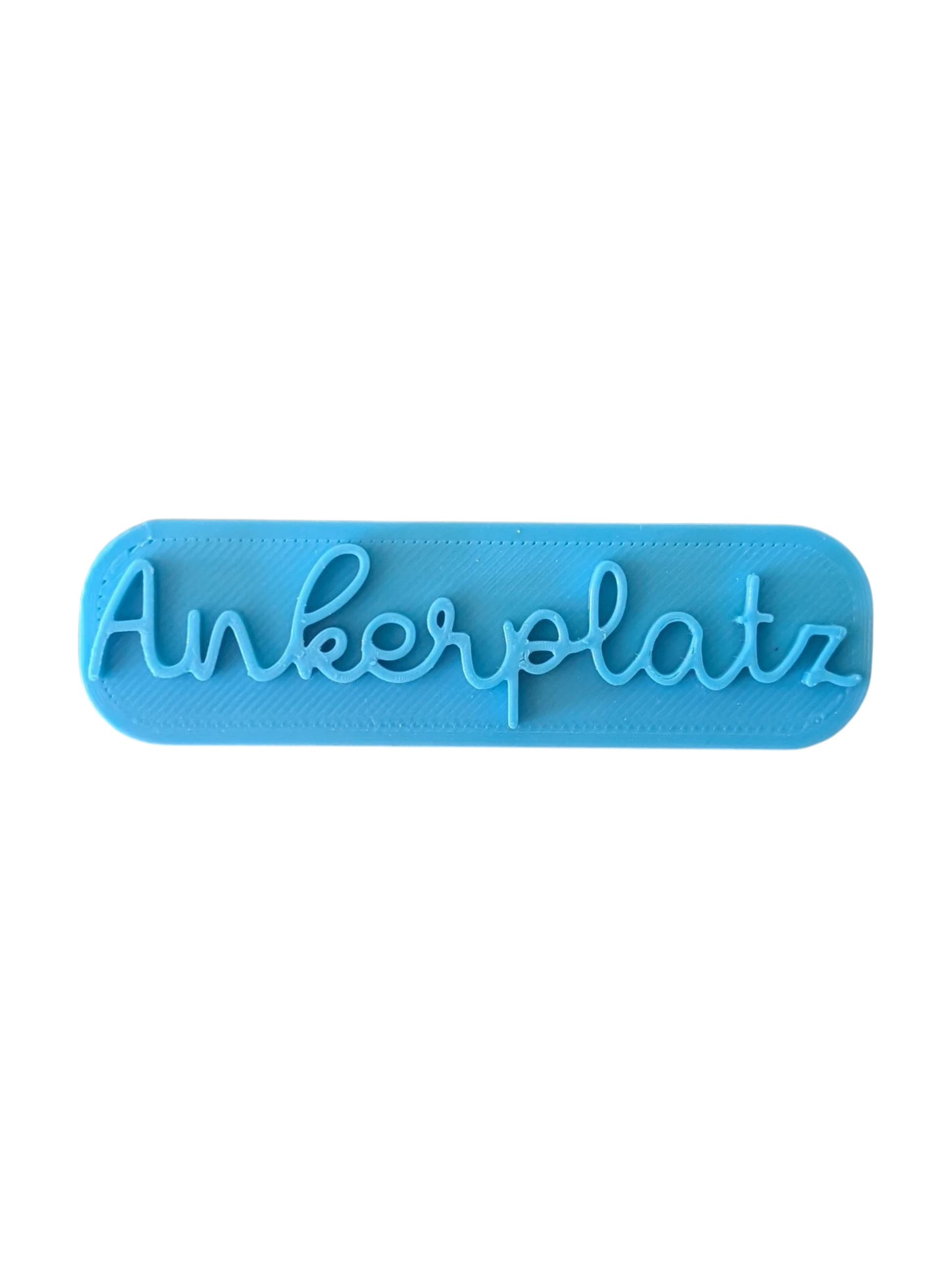 Draufsicht auf den türkisfarbenen Prägestempel für Ton mit dem Schriftzug 'Ankerplatz'. Ein eleganter Textstempel für maritim dekorierte Keramik und Türschilder.
