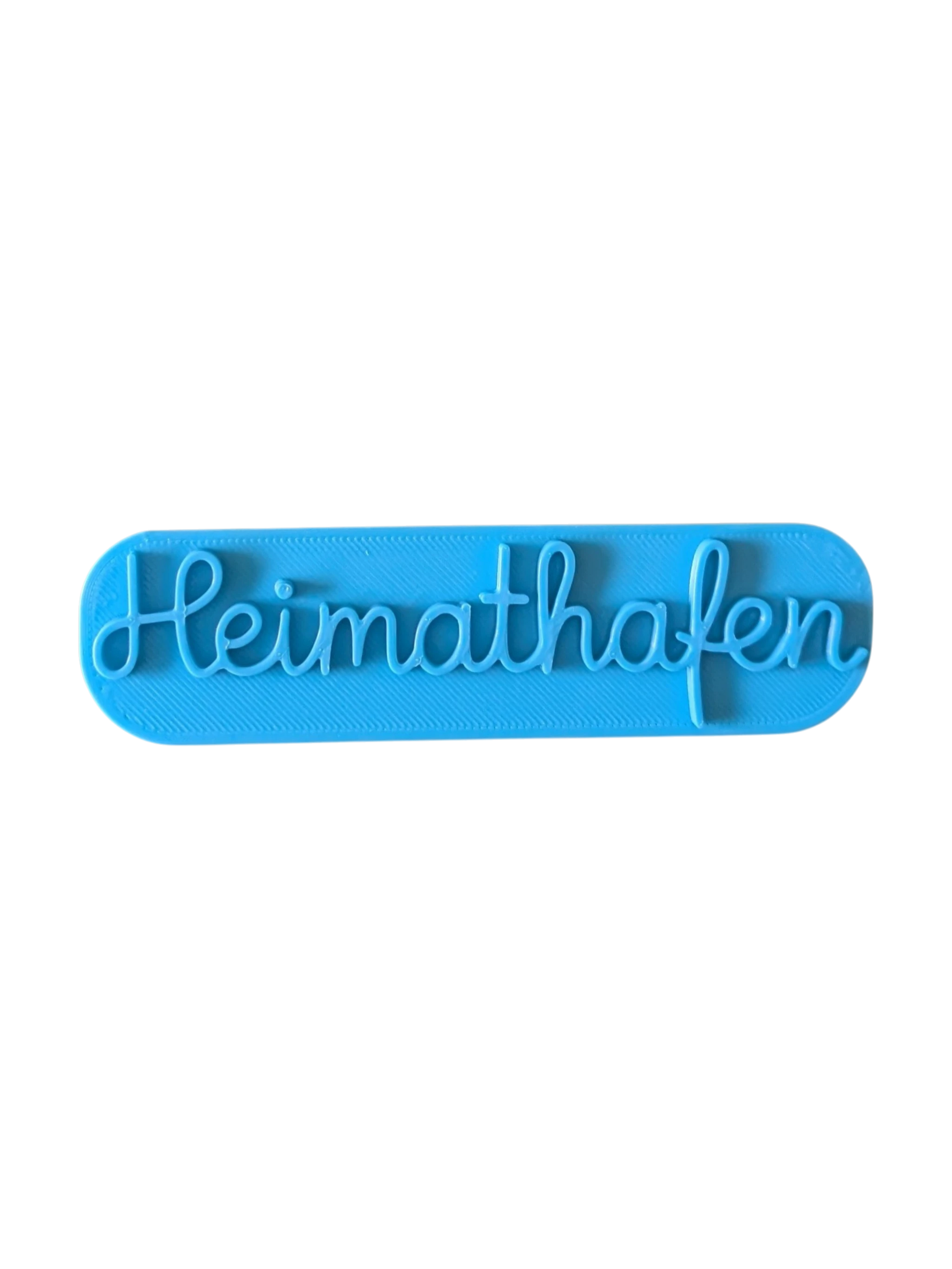 Draufsicht auf den türkisfarbenen Prägestempel für Ton mit dem Schriftzug 'Heimathafen'. Ein eleganter Textstempel für maritim dekorierte Keramik und Türschilder.