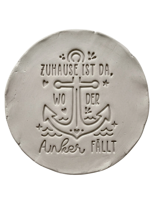 Präziser Stempelabdruck des maritimen Textstempels 'Zuhause ist da, wo der Anker fällt' in hellem Ton. Das tiefe Relief zeigt den Anker und die Schrift perfekt auf einer runden Tonplatte.