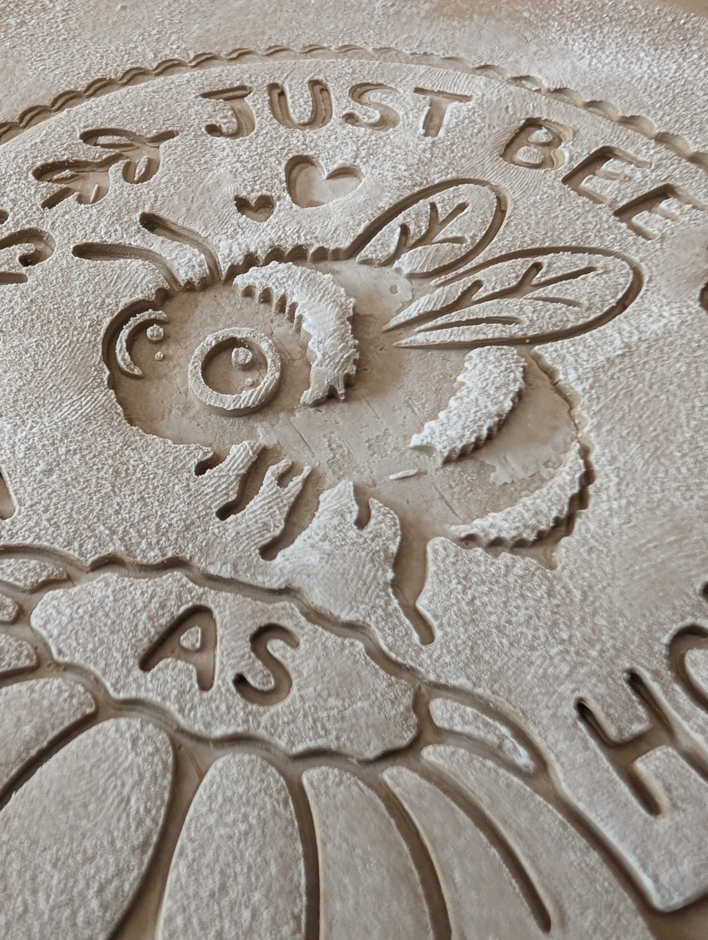 Sauberer Stempelabdruck des Bienen-Motivs in unglasiertem Ton, leicht bemehlt. Die feinen Details der Biene, der Blüte und der Schrift kommen auf der Tonplatte wunderschön zur Geltung.