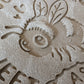 Sauberer Stempelabdruck des Bienen-Motivs in unglasiertem Ton, leicht bemehlt. Die feinen Details der Biene, der Blüte und der Schrift kommen auf der Tonplatte wunderschön zur Geltung. Foto einer Nahaufnahme