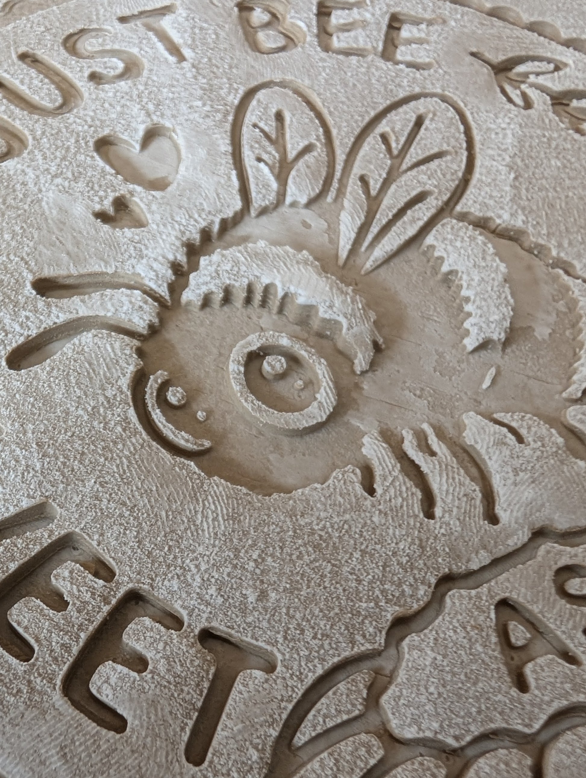 Sauberer Stempelabdruck des Bienen-Motivs in unglasiertem Ton, leicht bemehlt. Die feinen Details der Biene, der Blüte und der Schrift kommen auf der Tonplatte wunderschön zur Geltung. Foto einer Nahaufnahme